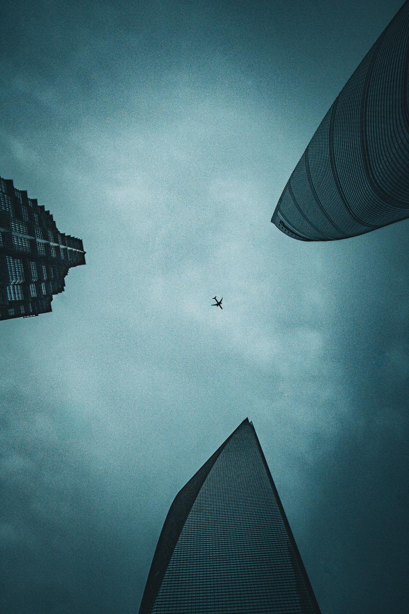Airplane flying between Shanghai skyscrapers against teal sky