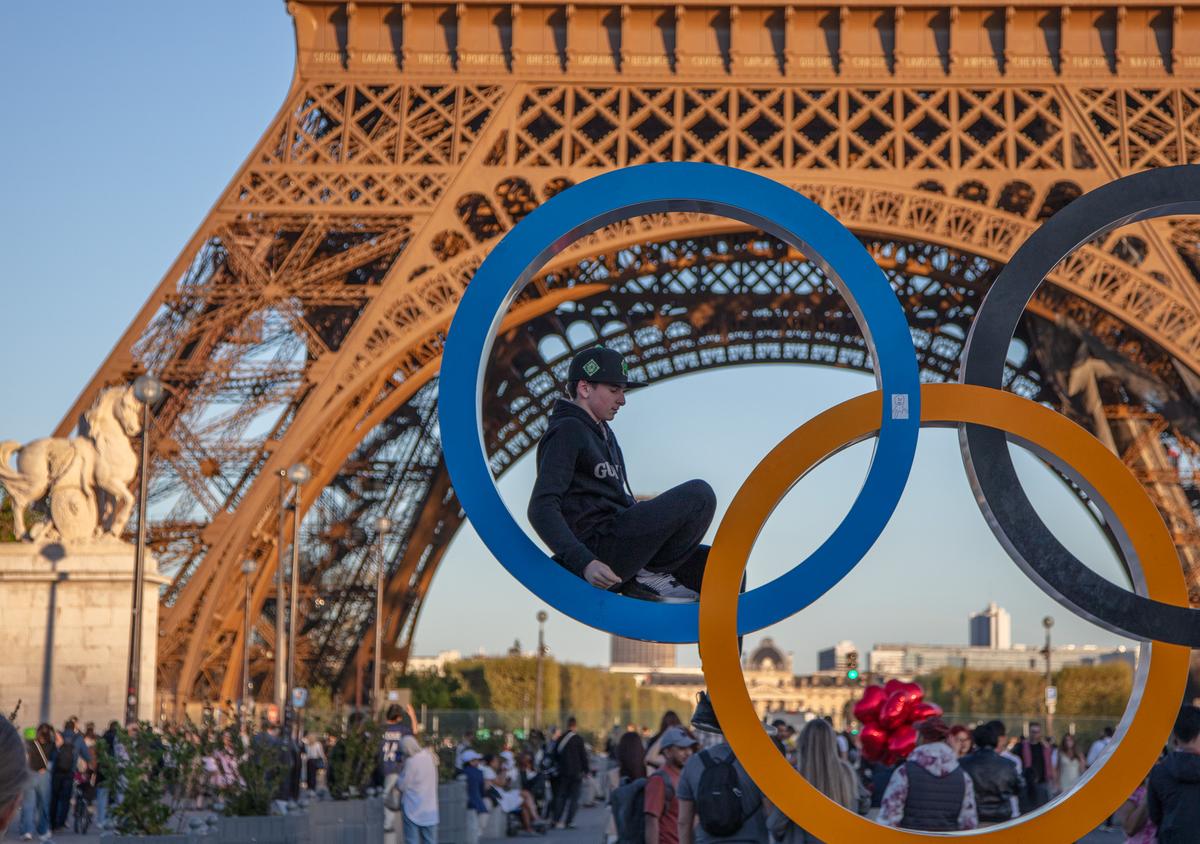 Person posing inside Olympic rings beneath the Eiffel Tower
