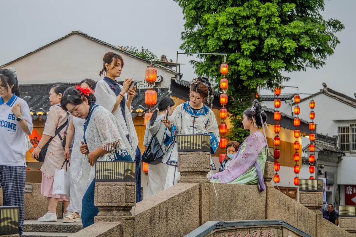 Women in hanfu crossing a lantern-lit stone bridge in Suzhou
